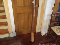 Didgeridoo standing upright, full length shown with visible natural wood grain and slight curve.