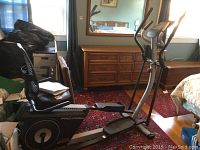 Side angle showing full elliptical machine with pedals, seat, and handles indoors on carpet.