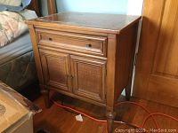 Wooden night table showing front view with drawer and two rush-front cabinet doors, minor finish wear on top surface