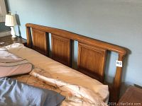 Photo showing full view of queen wooden headboard mounted to bed, with visible three molded rectangular panels and curved top edge.