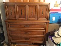 Frontal photo showing entire dresser with four molded wooden doors on top and three drawers below with metal handles.