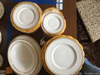 Top down view of stacked plates and serving bowls showing the gold lace pattern on white china with yellow protective fabric between pieces.