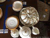 Tea cups arranged in round container beside stacked saucers, teapot, sugar bowl lid visible