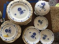 Stack of dinner plates and smaller plates with blue floral decoration along with two serving bowls and covered tureen shown from above.