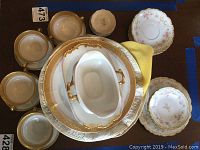 Photo showing assortment of Limoges china including dinner plates, bouillon cups, underplates, and sauce boat with gold trimming and fine porcelain detail.