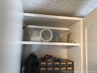 Photo of wall cupboard interior showing drawer unit with multiple small labeled drawers for nuts, bolts and other small hardware alongside a large black container