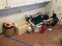 Mickey Mouse themed storage boxes, pink watering can, ceramic pots, laundry basket with garden tools, and fire extinguisher arranged on garage floor.