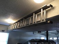 Photo of Keller brand metal extension ladder mounted horizontally near ceiling in garage.