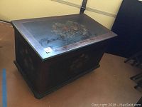 Front angled view of the wood chest showing floral painted top and front panel with some wear.