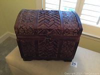 Closed view of small decorative wooden chest with ornate geometric pattern and latch, sitting on ottoman