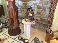Wide shot with Indian style petal stand with chef figurine on top, flanked by wood carvings and decorative objects.