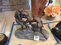 Photo showing front and right side angle of the bronze sculpture with four human figures on the base.