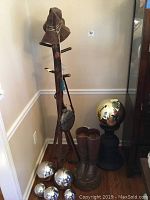 Photo of the faux wood coat rack, cowboy boot umbrella stand, leather hat, decorative canteen, and metal decorative spheres arranged in corner of room.