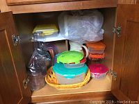 Plastic containers with lids stored inside wooden kitchen cabinet.