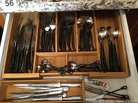 Drawer organizer with black handled forks, knives, spoons, and additional silverware items