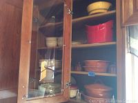 Kitchen cabinet shelf with various Rachel Ray stoneware in red and orange, including bowls and covered dishes