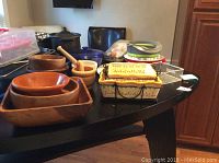 Wide view of collection on dark wood table showing wood bowls, wooden mortar and pestle sets, casserole dishes, metal racks, and plastic containers.