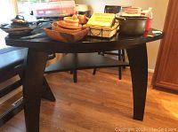 Photo showing tear drop-shaped high top table with angled legs and some kitchenware on top, table resting on hardwood floor.