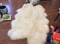 Large white fluffy sheepskin rug with petal-shaped edges spread on hardwood floor