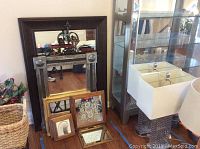 View of large dark wood framed mirror with mounted metal cross along with several smaller framed mirrors on the floor in front of it