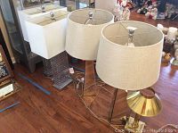 Four contemporary table lamps with varied bases and shades arranged on hardwood floor.