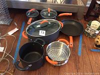 Full view of cookware set showing saucepans with lids, Dutch oven, skillet, and steamer insert with orange handles.