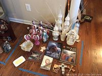 Wide shot showing entire collection spread on hardwood floor, including faith angels, Mother Mary statues, decorative glass finials with gold branches, crosses, and books.