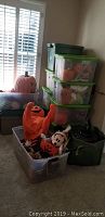 Stacked plastic tubs and various Halloween decorations visible around, including a large pumpkin with black hat.