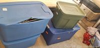 Four packed storage tubs in blue and green plastic with lids, containing untested Christmas decorations.