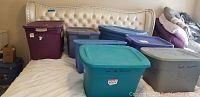Photo showing seven plastic storage tubs of various colors placed on a bed, packed and closed, holding the lot contents.