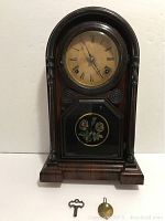 Front view of clock with floral bottom glass, showing original pendulum and key placed in front.