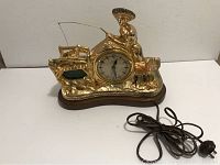 Full view of the gold-tone animated fish clock with power cord visible, showing the fisherman holding a fishing pole and clock face in the center.