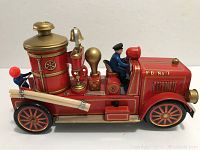 Left side profile of vintage red tin toy fire engine with driver figure, showing bell and hose details