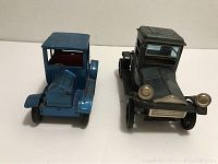 Front view of two vintage tin toy cars: black Bandai 1918 Packard on right and blue car on left.