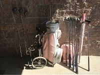 Photo of full golf set including clubs, bag, umbrella, and cart against a brick wall.