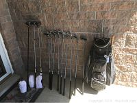 Full view of set showing all clubs and bag arranged against wall, clubs from woods to putter and bag on right side.