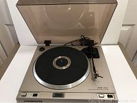 Full view of the Marantz TT 2000 turntable with dust cover, showcasing metallic base and black platter with the power cord and connectors in back.