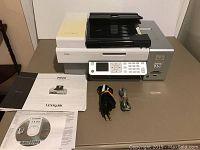 Lexmark X7550 printer with power cord, USB cable, and manuals laid out on table