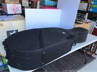 Black full size cello case on wheels placed on a table, showing overall shape and size suitable for a cello.