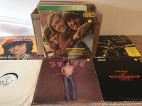 Photo showing a boxed set of LP records with visible covers including The Monkees, Elvis Presley, and individual LPs laid out such as John Travolta and Frank Mahon.