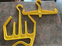 Two yellow plastic hangers with multiple prongs and hooks placed on a surface, designed for diving equipment.