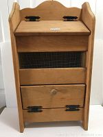 Front view of wooden vegetable bin showing the hinged top lid, mesh ventilation, and bottom drawer with wooden knob and black hinges.
