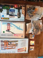 Photo shows unopened or partially opened boxes of model kits including Faller container crane, IHC gantry crane, and Walthers Cornerstone kits. Various assembled parts in sealed bags visible.