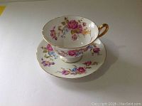 Side and top view of Shelley floral tea cup sitting inside matching saucer showing detailed pattern and gold trim.