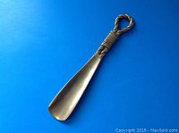 Full view of the brass shoe horn showing the length and overall shape against a blue background.