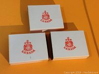 Three white cardboard sleeves with red Canadian coat of arms and 'CANADA' text, stacked together