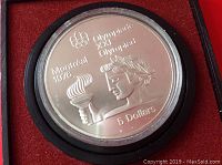 Close-up of the silver coin showing the torch bearer, Olympic flame, and inscriptions including 'Montreal 1976' and '5 dollars'.