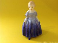 Porcelain figurine of a young girl named Marie wearing a detailed purple and blue dress, standing pose.