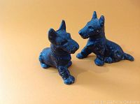 Two black cast iron Scotty dog figurines placed side by side on orange background.