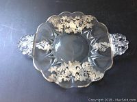 Full view of clear glass serving dish with two decorative handles on each side and sterling silver overlay designs of birds and grapevines.